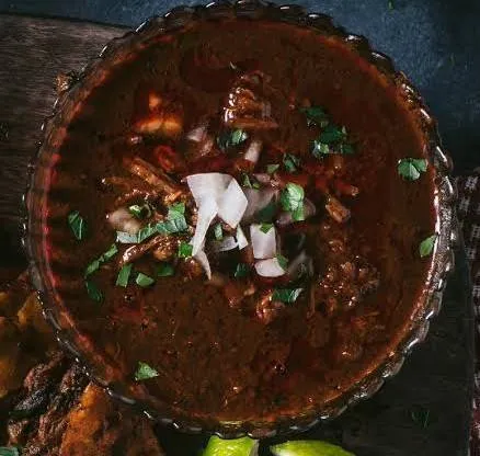 Cazuela de barro con birria de res, cilantro y cebolla, vista desde arriba.