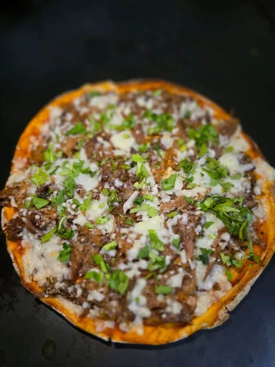Pizzabirria individual con queso derretido, carne de birria y cilantro, sobre la plancha negra.