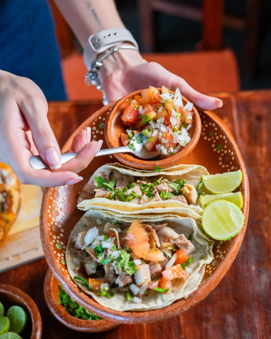 Tacos servidos en plato de barro pintado, con pico de gallo y limones.